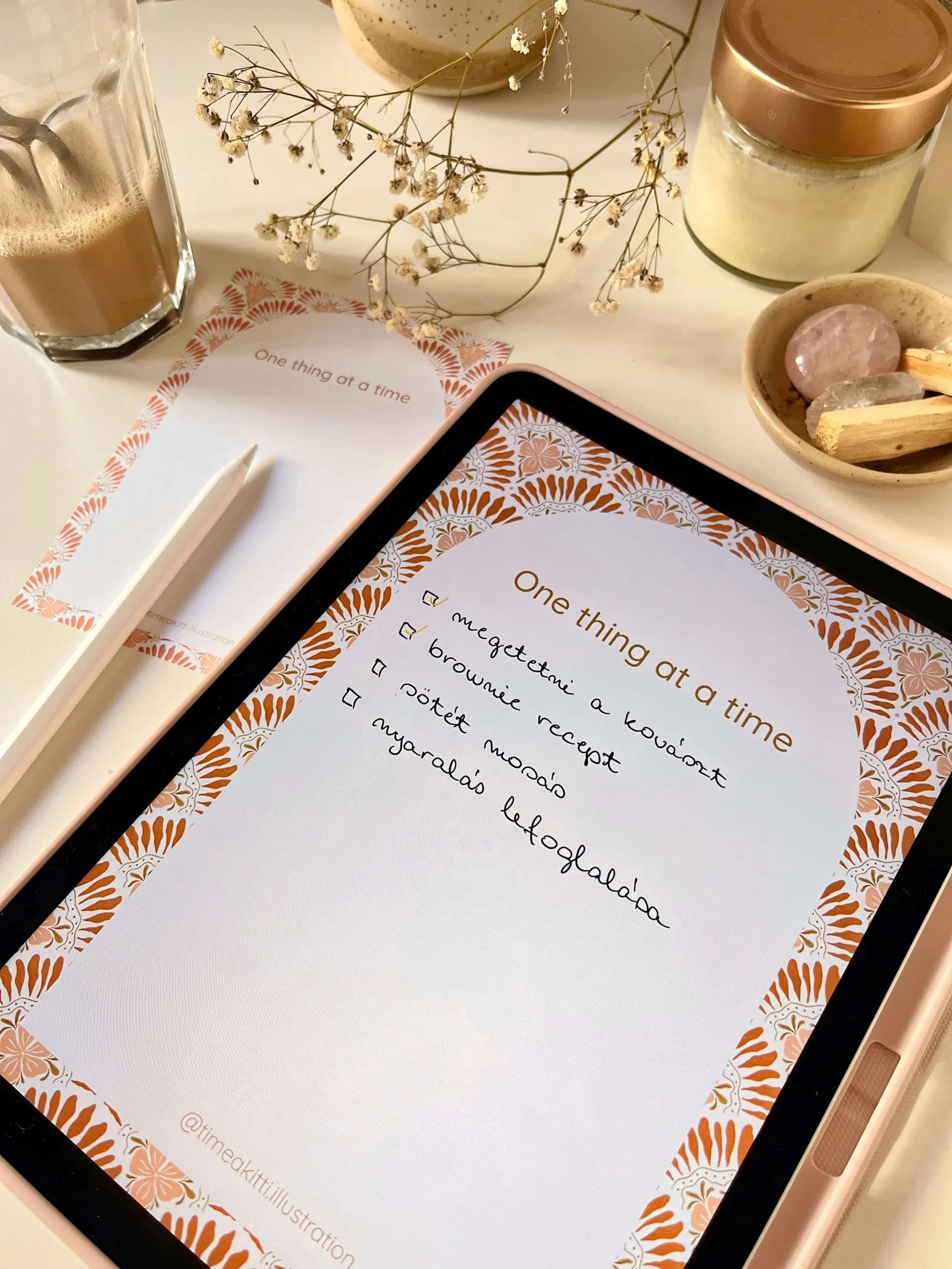 Rózsaszín és terrakotta virágmintás digitális jegyzetlap, iPaden megnyitva és nyomtatott változatban is, kávé és íróeszköz mellett.