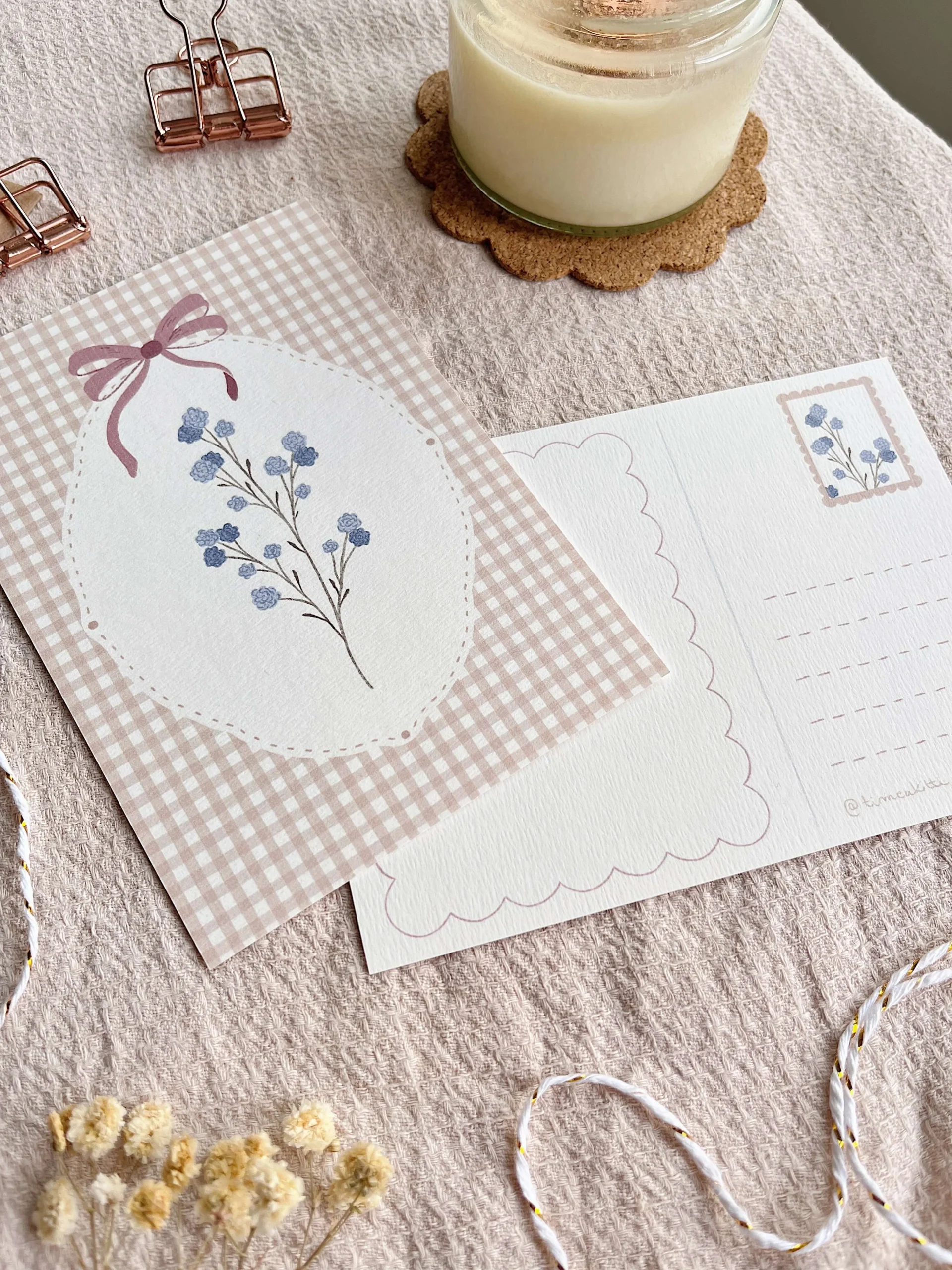 Cottagecore hangulatú őszi képeslap. A kézzel illusztrált print háttere barna gingham mintás, rajta fehér keretben és lila masnival és finomka rezgő. A képeslap hátoldalán külön kialakított hely van a címzésnek és a bélyegnek. A fotón szerepel még gyertya és boríték is. Kuckózós hangulat levelezéshez.